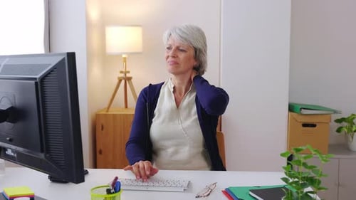 Middle Age Businesswoman with Neckache Sitting at Desk at Home Office