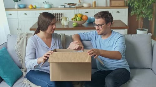 Couple Opening Cardboard Box Together on Sofa at Home