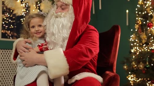 Little Girl Sitting with Santa and Holding Gift