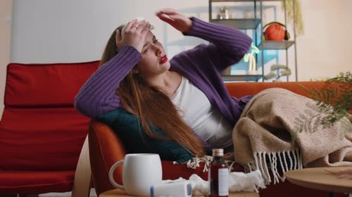 Jeune femme malade souffrant d'allergie au froid, allongée sur le canapé de la maison, éternuant, essuie de la morve dans une serviette
