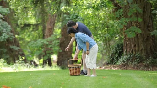 Mature asian couple preparing a relaxing picnic in the summer park together