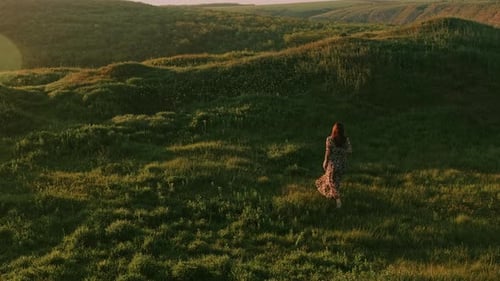 Lone Woman Walking Through Lush Green Hills at Golden Hour