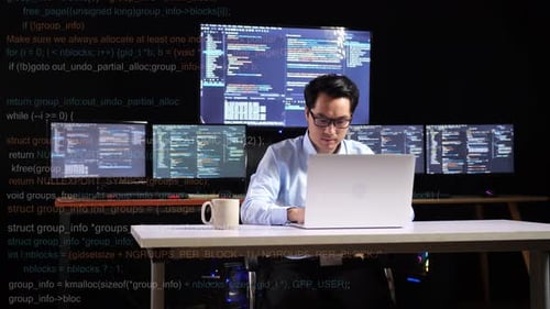 Asian Male Programmer Writing Code By A Laptop Using Multiple Monitors Showing Database