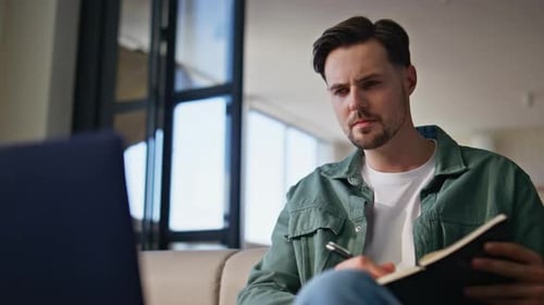 Young Adult Writing in Notebook with Laptop Nearby