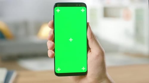 Close-up of a Man's Hand Holding Green Mock-up Screen Smartphone. Modern Mobile Phone. In the Backg