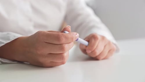 A Woman's Hands Hold a Cap and a Pen on a White Table