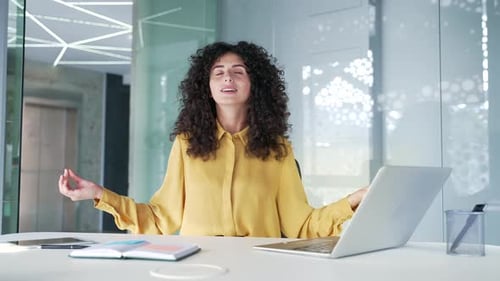Young adult businesswoman is meditating with her eyes closed sitting at workplace in office. Female