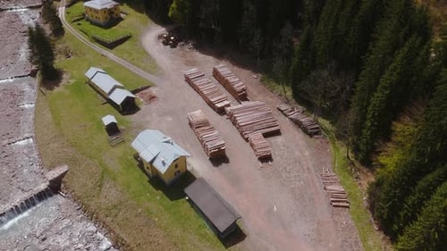 Ein Sägewerk in einem Waldgebiet mit Stapeln geschnittener Baumstämme und sichtbaren Gebäuden, Luftaufnahme