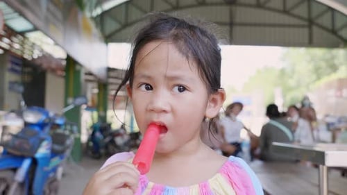 Happy Asian little girl eating popsicle at summertime