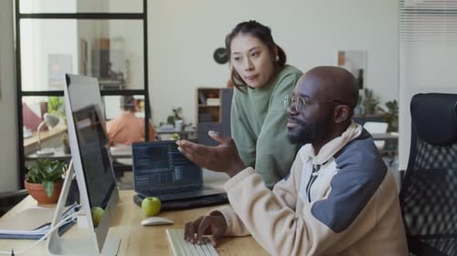 Schwarzer männlicher Programmierer beschwert sich bei einer asiatischen Kollegin über einen Fehler im Code