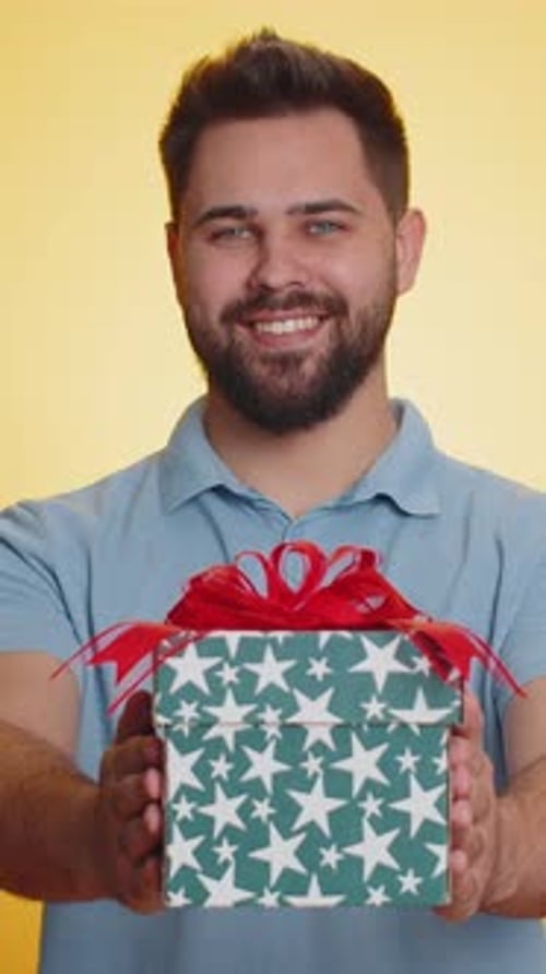 Smiling Man Holding Out Wrapped Present on Yellow