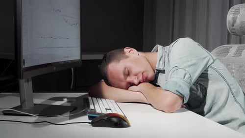 Tired Young Adult Sleeping at Desk Next to Computer