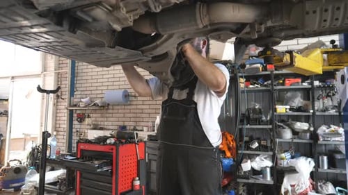 Professional Mechanic Working with a Lifting Vehicle at Auto Service