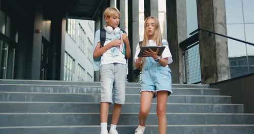 Two teenage students boy girl friends using digital tablet computer exchange lectures near school