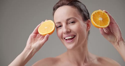 Smiling Woman Holding Orange Slices Over Eyes