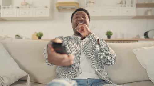 Smiling Young Adult Using Remote Control on Couch