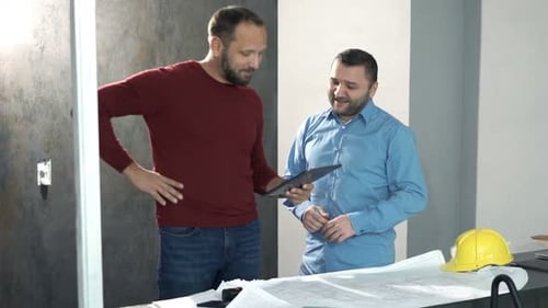 Men Review Blueprints with Tablet in Office