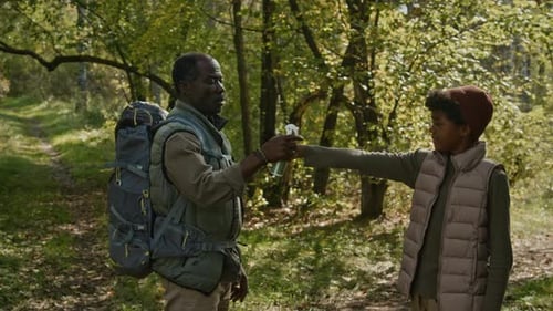 Father Spraying Repellent on Teenage Boys Clothes during Hike in Woods