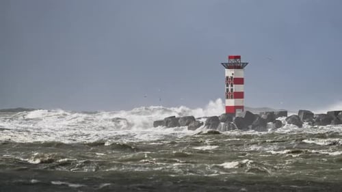Storm waves crash over lighthouse at harbor entrance; IJmuiden, Netherlands
