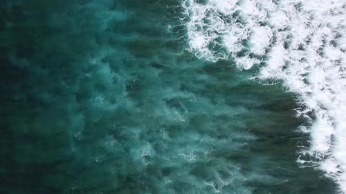 Stormy sea with waves breaking, white foam and beach sand dragged into the sea