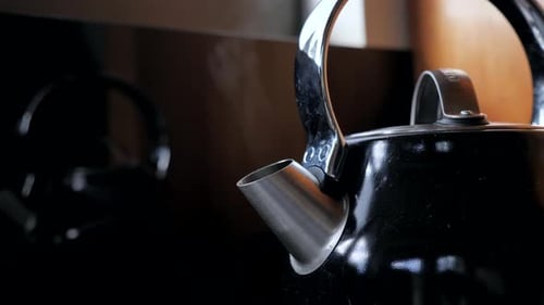 Fixed shot of black household domestic kitchen kettle slowly boils for cup of tea coffee with steam