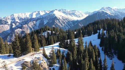 Aerial View of Winter Mountain Forest on a Sunny Day with Huge Snowcapped Mountains in the