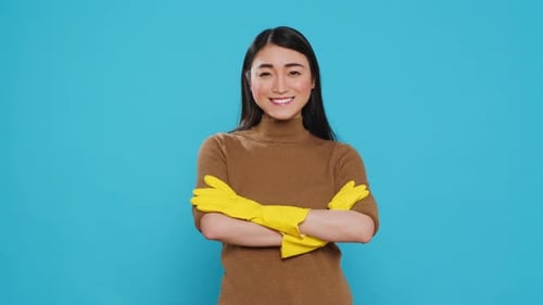 Smiling Professional Maid Wearing Protective Rubber Gloves Standing with Arm Crossed in Studio