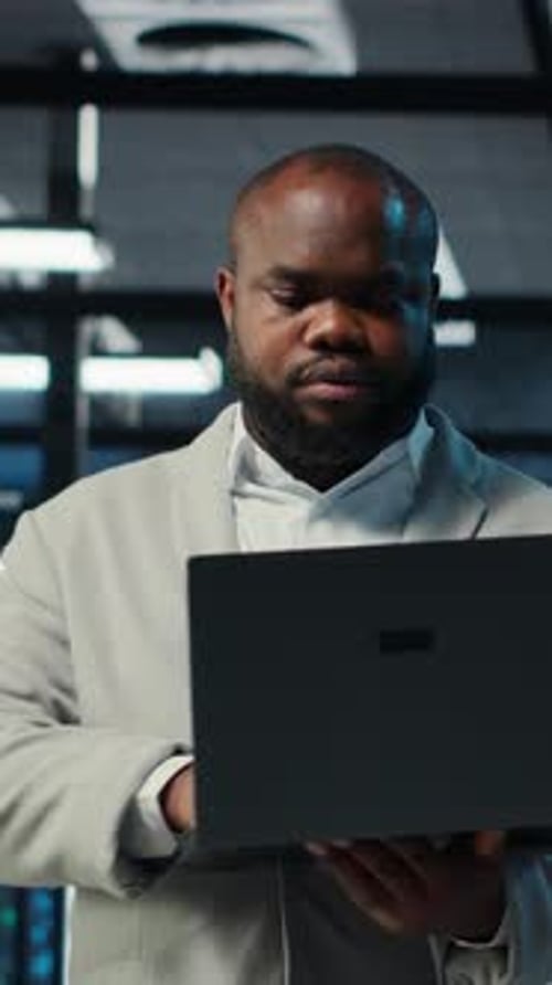 Man Uses Laptop in Front of Server Racks