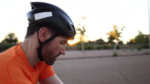 Cyclist slowly turning head while cycling on road at sunset