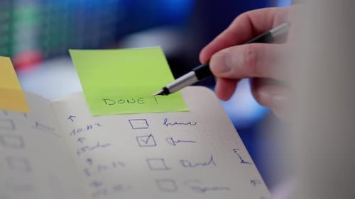 Hand Checking Off To-Do List with Pen in Notebook