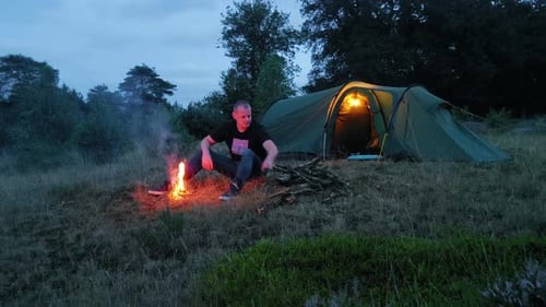 Man Camping with Tent and Campfire in Rural Setting