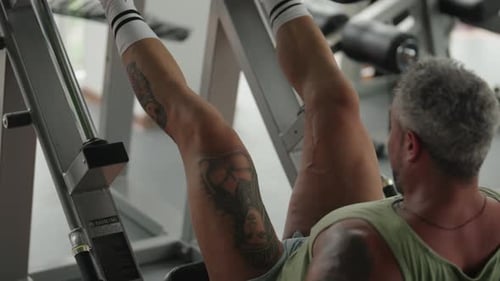 Tattooed Man Exercising on Leg Press Machine at Gym