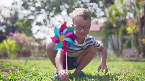 Boy in glasses is playing with pinwheel in a garden