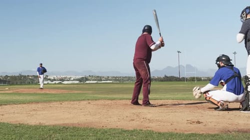 Playing baseball, batter in maroon uniform preparing to hit pitch on field