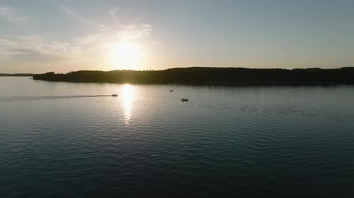 orbiting drone shot of the silhouettes of fishing boats and pontoons on a lake at sunset