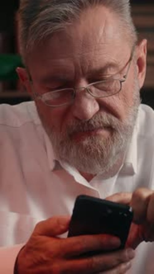 Serious Caucasian Old Senior Retired Business Man Using Mobile Phone Touching Screen at Office