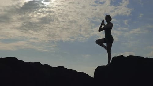 Woman Doing Yoga on Rocky Coast at Sunrise