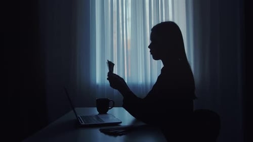 Silhouette of Person Counting Money with Glass of Water on Table