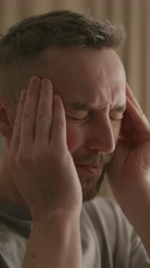 Man Experiencing Headache Massages Temples in Indoor Setting