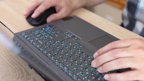 02Close-up of hands using a laptop keyboard and mouse on a wooden desk. Work, internet browsing, and
