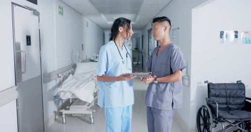 Diverse doctor and nurse using tablet and talking in corridor at hospital, in slow motion
