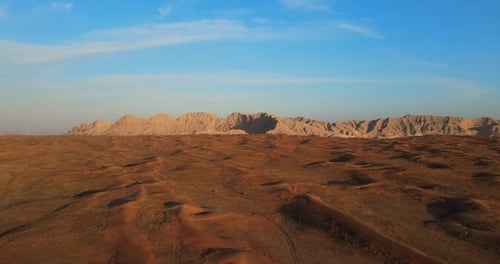 Aerial Cinematic View of Golden Desert Dunes and Rugged Mountain Peaks