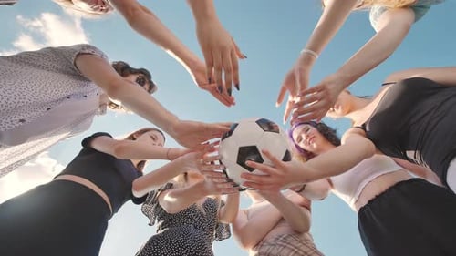 Group of Young Women Forming a Circle Around a Soccer Ball with Their Hands Viewed From a Low Angle