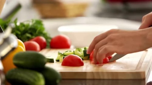 Hands slice ripe tomato on cutting board