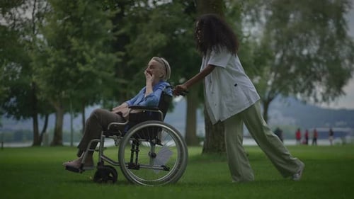 Woman pushes senior in wheelchair through green park