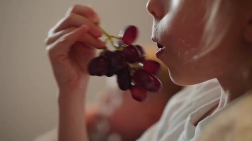 Close Up of Young Girl Eating Grapes with Blurred Figure in Background