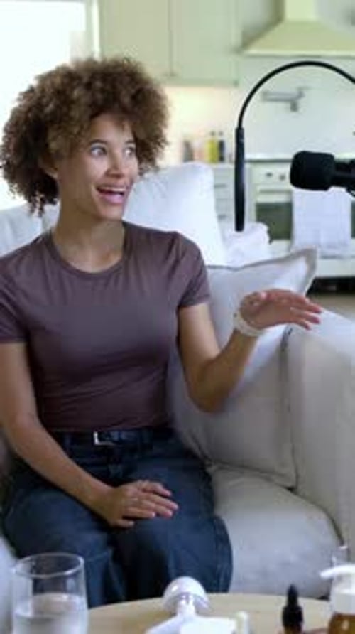 Vertical video: Facing mic, creator wearing brown tee gesturing, reviewing amber bottles on couch