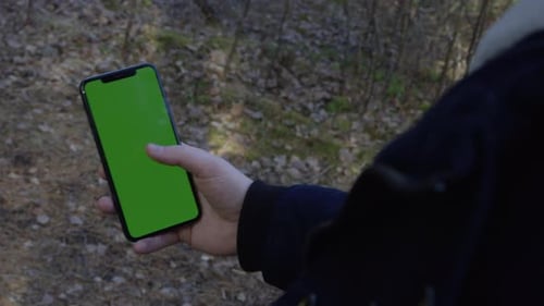 Hand tapping and swiping up on cell phone in the woods with chroma key green screen