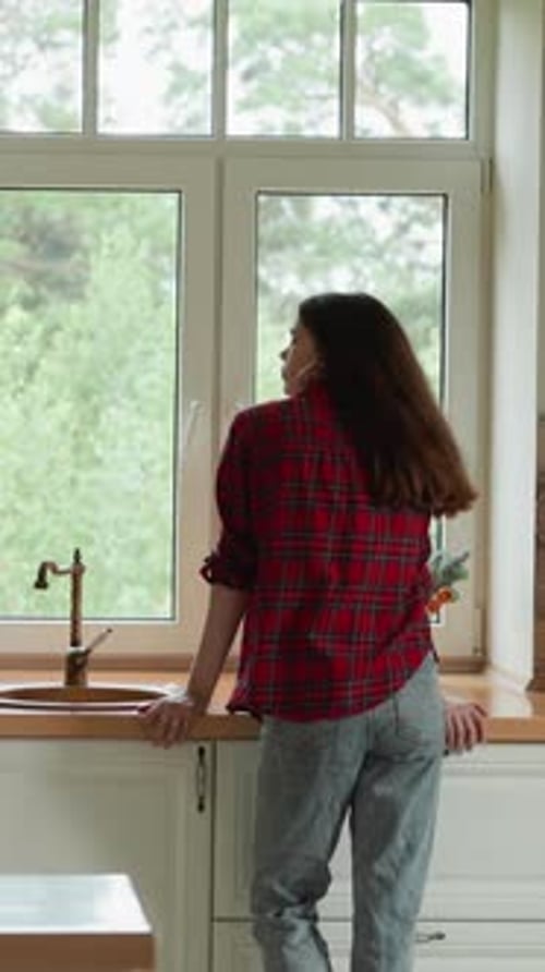 Woman Gazing Out Window in Bright Kitchen