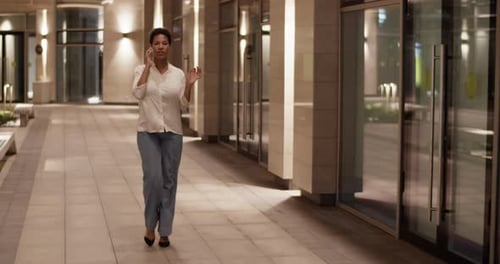 Black Businesswoman Walking Outside Modern Business Center and Talking on Mobile